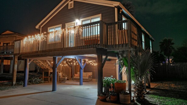 Ein zweistöckiges Haus mit überdachter Veranda, Lichterketten und Blumentöpfen.