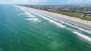 Luftaufnahme einer Küstenstadt mit einem langen Strand, blauem Himmel und einer Mischung aus Wohn- und Geschäftsgebäuden.