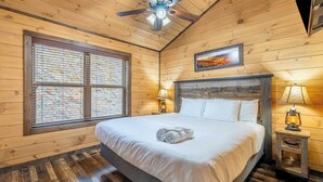 Una camera con pareti in legno, un letto, due lampade da comodino, una ventola a soffitto e una finestra con tende.