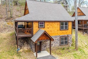 A cabin with a porch, a deck, and a stone foundation. - The Wacky Woodpecker by Avantstay Game Room, Private Hot Tub, & Pool Access! (Pigeon Forge)