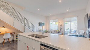 A modern kitchen with a built-in dishwasher, a dining area with a table and chairs, and a staircase. - Zanjero by Avantstay Mins From Downtown Palm Springs Private Terrace, Shared Pool (Palm Springs)