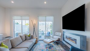 A modern living room with a sofa, a chair, a fireplace, and large windows.