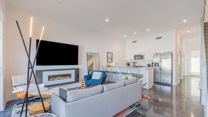 A modern living room with a flat-screen TV, a fireplace, a sofa, and a dining area with chairs. - Zanjero by Avantstay Mins From Downtown Palm Springs Private Terrace, Shared Pool (Palm Springs)