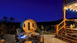 A wooden cabin with a circular window, outdoor seating with Adirondack chairs, a fire pit, and a staircase leading to an upper deck. - Modern Timber- Hot tub, sauna, theatre, climb wall (Beaver Mines)