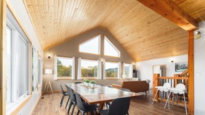 A spacious dining area with a wooden table and chairs, large windows, and a high ceiling. - Modern Timber- Hot tub, sauna, theatre, climb wall (Beaver Mines)
