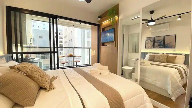 Ein Hotelzimmer mit einem großen Bett, einem kleineren Bett, einem Balkon mit Tisch und Stühlen, einem Fernseher und einem Deckenventilator.