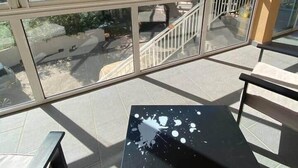 A balcony with a glass railing, a black table with a white splatter, and a view of trees and a staircase.