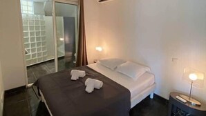 A hotel room with a bed, a nightstand, a lamp, a sliding glass door to a balcony, and an air conditioning unit.