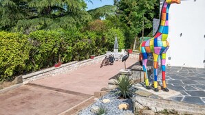A colorful giraffe statue in front of a white building with a stone pathway and greenery. - LA Girage DE BEL AIR (Amboise)