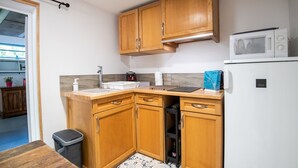 A compact kitchen with wooden cabinets, a microwave, a sink, and a trash bin. - LA Girage DE BEL AIR (Amboise)