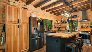 Eine holzgetäfelte Küchenzeile im Blockhausstil mit Kochinsel, Edelstahlgeräten und einer Pendelvorrichtung für Kochutensilien.
