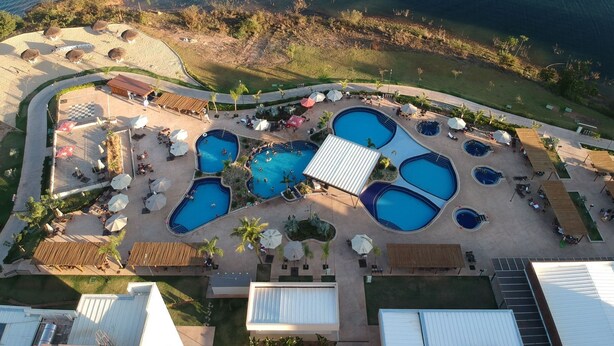 Luchtbeeld van een resort met meerdere zwembaden, ligbedden en een strandgedeelte.