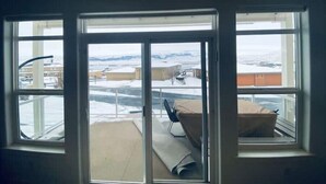 Ein Zimmer mit drei Fenstern, einem Bett mit Matratze und Kissen sowie Blick auf eine verschneite Landschaft mit Gebäuden.