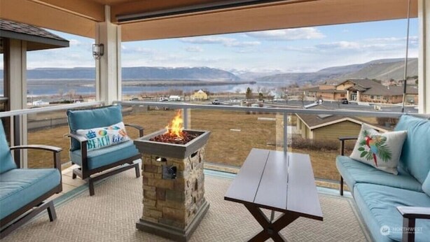 Ein Balkon mit Steinkamin, Sitzgelegenheiten und Blick auf einen See sowie entfernte Gebäude.