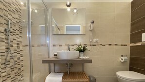 A modern bathroom with a glass shower enclosure, a sink with a mirror above, a toilet, and a trash bin. - Porta Alla Croce Guest House (Florence)