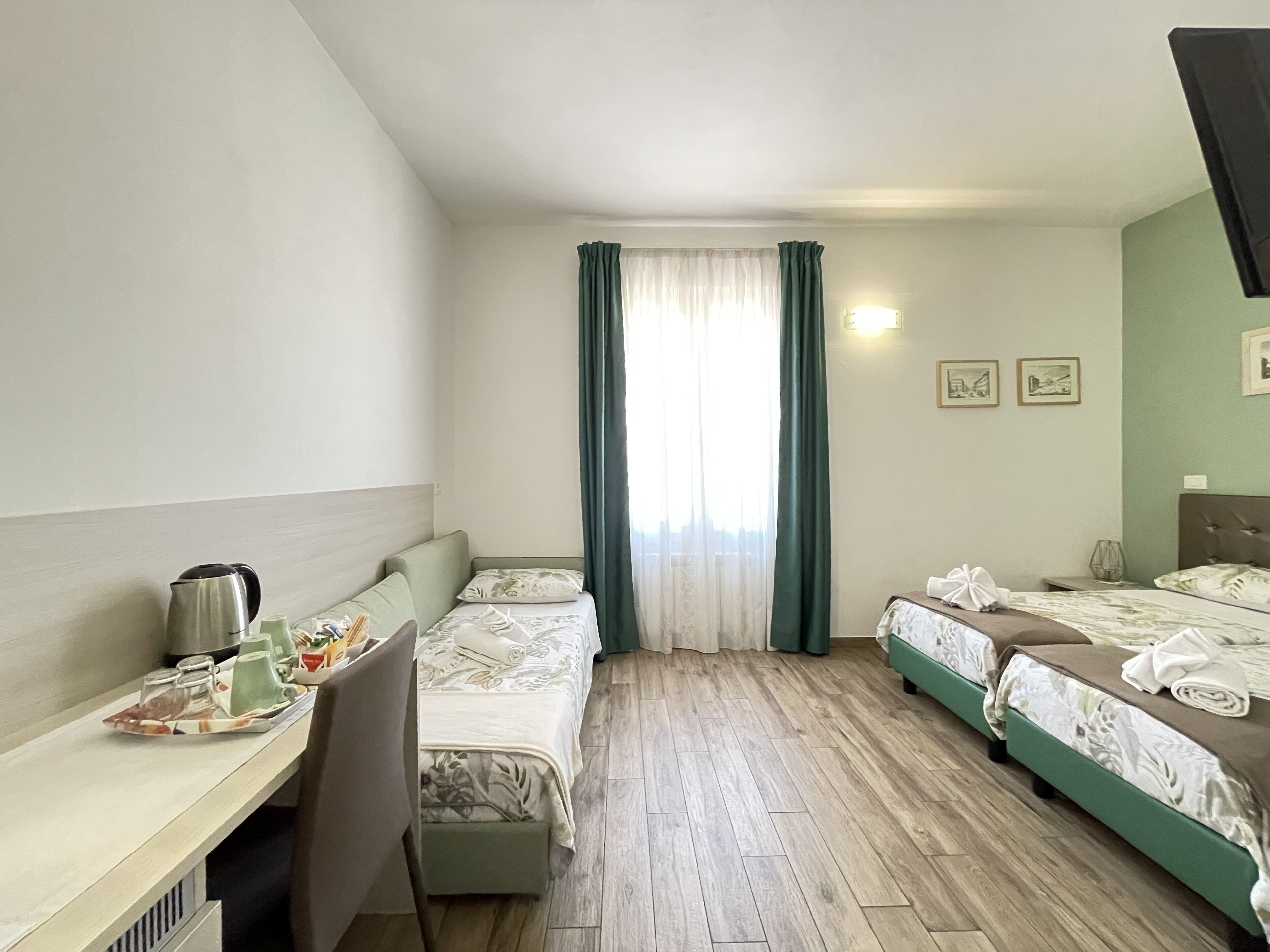 A hotel room with two single beds, a desk with a kettle, and a window with curtains.