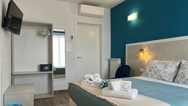 A hotel room with a bed, a TV, a mirror, a window, and a wall-mounted light. - Porta Alla Croce Guest House (Florence)