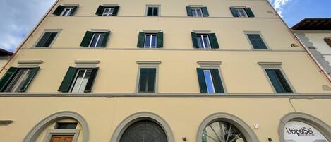 A multi-story building with a beige facade, green shutters, and a sign for UnipolSai Assicurazioni.