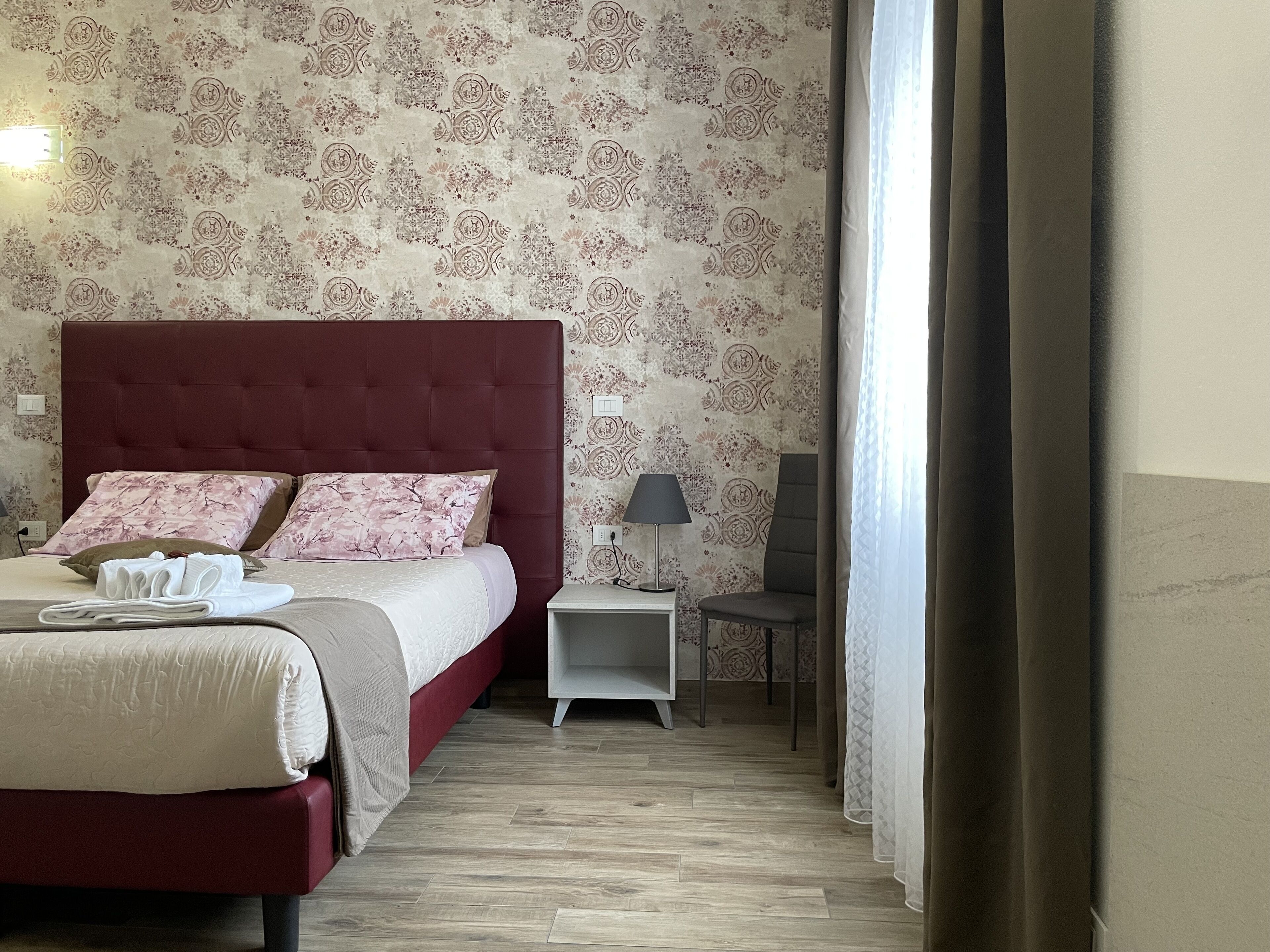 Un lit bien fait, avec une tête de lit rouge, une table de chevet avec une lampe et une chaise.