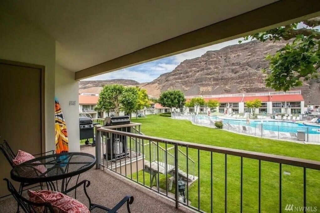 A balcony with a view of a swimming pool, a grassy area, and a mountain in the background.
