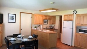 A compact kitchen with wooden cabinets, a central island, a dining table with chairs, and a refrigerator. - #155- Kater's Kabin Condo near large pool & shuttle to Gorge Amp-book separately (Quincy)