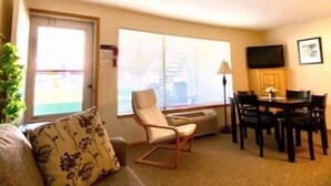 A living room with a sofa, a chair, a dining table with chairs, a TV, and a window with a view. - #155- Kater's Kabin Condo near large pool & shuttle to Gorge Amp-book separately (Quincy)