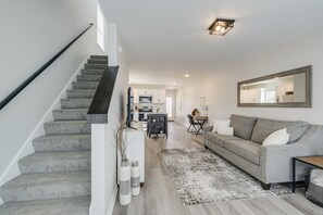 A modern living room with a staircase, a grey sofa, a coffee table, and a dining area in the background.