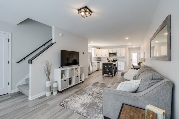 A modern living room with a grey sofa, a flat-screen TV, and a staircase leading to another level.