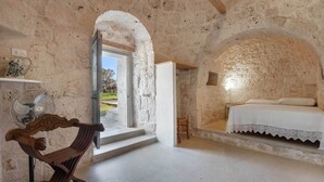 A rustic room with stone walls, a wooden bench, a bed with a white bedspread, and a small table. - 3745 Trullo Puspo by Barbarhouse (Carovigno)