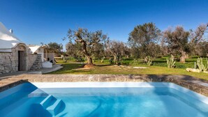 A swimming pool with a stone border, a stone building, and trees in the background. - 3745 Trullo Puspo by Barbarhouse (Carovigno)