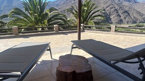 A terrace with two lounge chairs and a wooden stool, overlooking a mountainous landscape with palm trees. - Elqui Valley Avocado Farm, 2-bedroom cabin in fabulous Vicuña with WiFi (Vicuña)