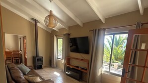 A living room with a sofa, a TV, a fireplace, and a balcony with a view of palm trees. - Elqui Valley Avocado Farm, 2-bedroom cabin in fabulous Vicuña with WiFi (Vicuña)