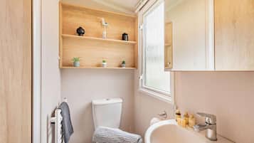 Une petite salle de bain comprenant des toilettes, un lavabo et des étagères en bois au-dessus des toilettes.