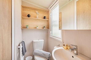 A compact bathroom with a toilet, a sink, and wooden shelves above the toilet.