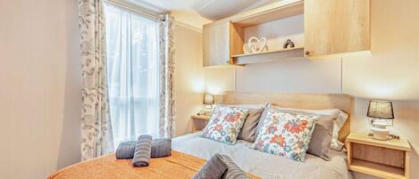 A neatly made bed with floral pillows, a wooden headboard, and a bedside table with a lamp.