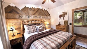 Een gezellig slaapkamer met een houten hoofdbord, een bed met geruit beddengoed, een nachtkastje met een lamp en een raam met uitzicht op bomen.