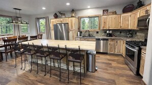 Een moderne keuken met houten kastjes, roestvrijstalen apparatuur, een groot eiland met barkrukken en uitzicht op de omgeving door grote ramen.