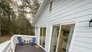 A deck with blue chairs and a table, a sliding glass door, and a white railing. - Cozy 2-bedroom 2 bath cottage in enjoyable Ocean Springs! Sleeps 4 guests. (Ocean Springs)