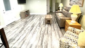 A living room with a wooden floor, a sofa, a coffee table, and a TV mounted on the wall. - Cozy 2-bedroom 2 bath cottage in enjoyable Ocean Springs! Sleeps 4 guests. (Ocean Springs)
