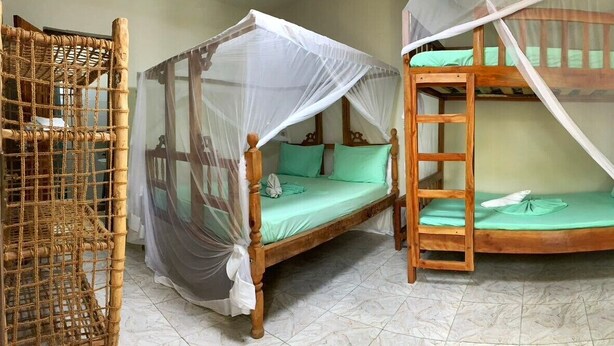 A room with a wooden bed with a canopy, a bunk bed, and a woven rattan chair. - Family room with balcon - Explore semplicity immerse yourself in nature  (Michamvi Kae)