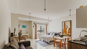 Moderni hotellihuone, jossa on sänky, työpöytä, ruokapöytä ja pieni keittiö.