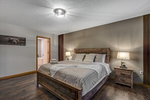 Una camera da letto con un letto in legno, due comodini con lampade, una porta che dà su un'altra stanza e un'opera d'arte appesa al muro.