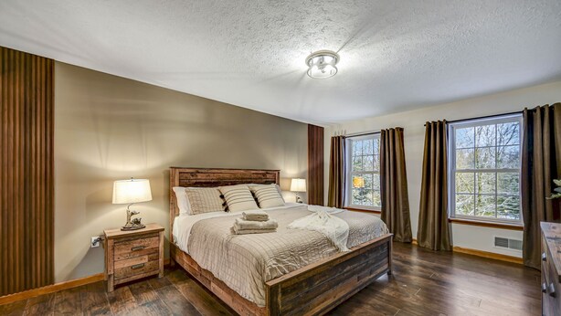 Een slaapkamer met een houten bed, een nachtkastje met een lamp en een raam met gordijnen.