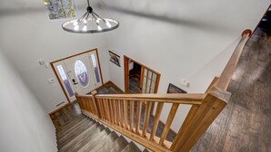 Een houten trap met een leuning, een hanglamp en een deur met een ruit.