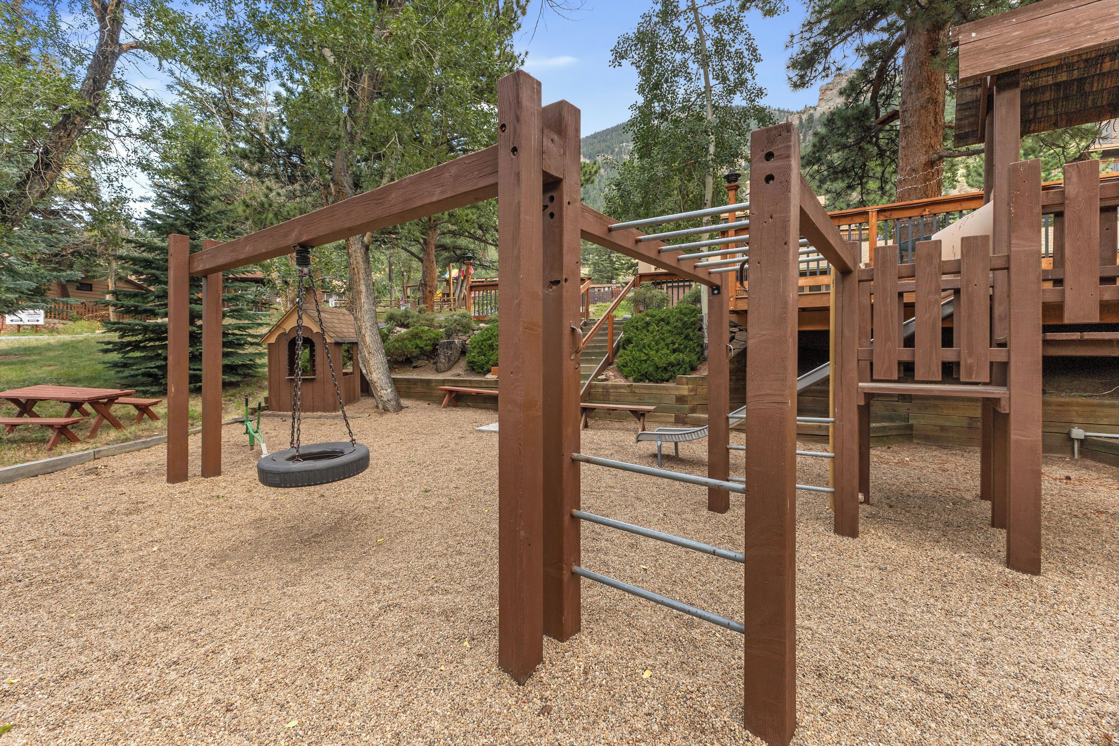 A wooden playground structure with a tire swing, picnic tables, and a small cabin-like shelter.