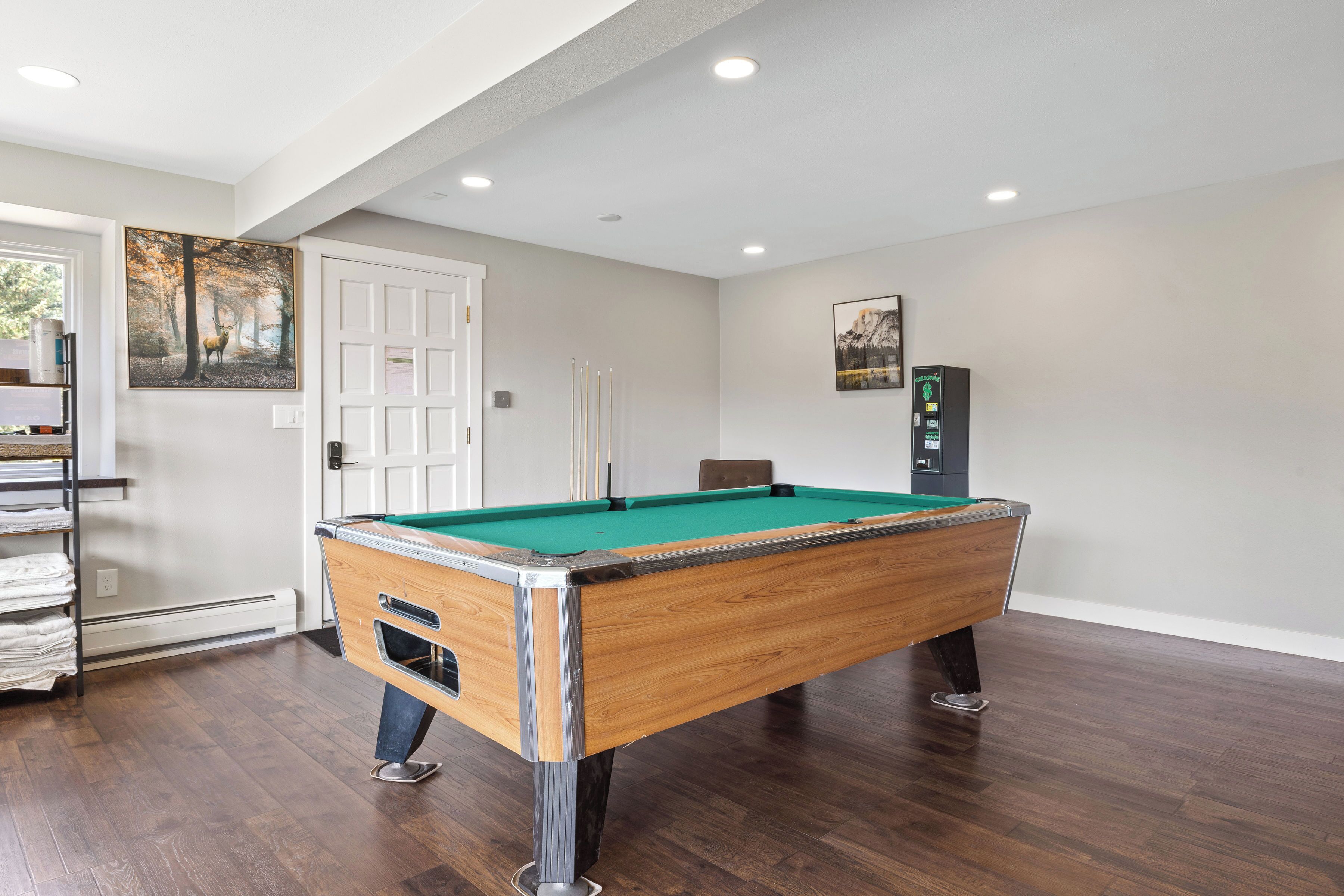 A pool table in a well-lit room with hardwood floors, a door, and a wall-mounted heater.