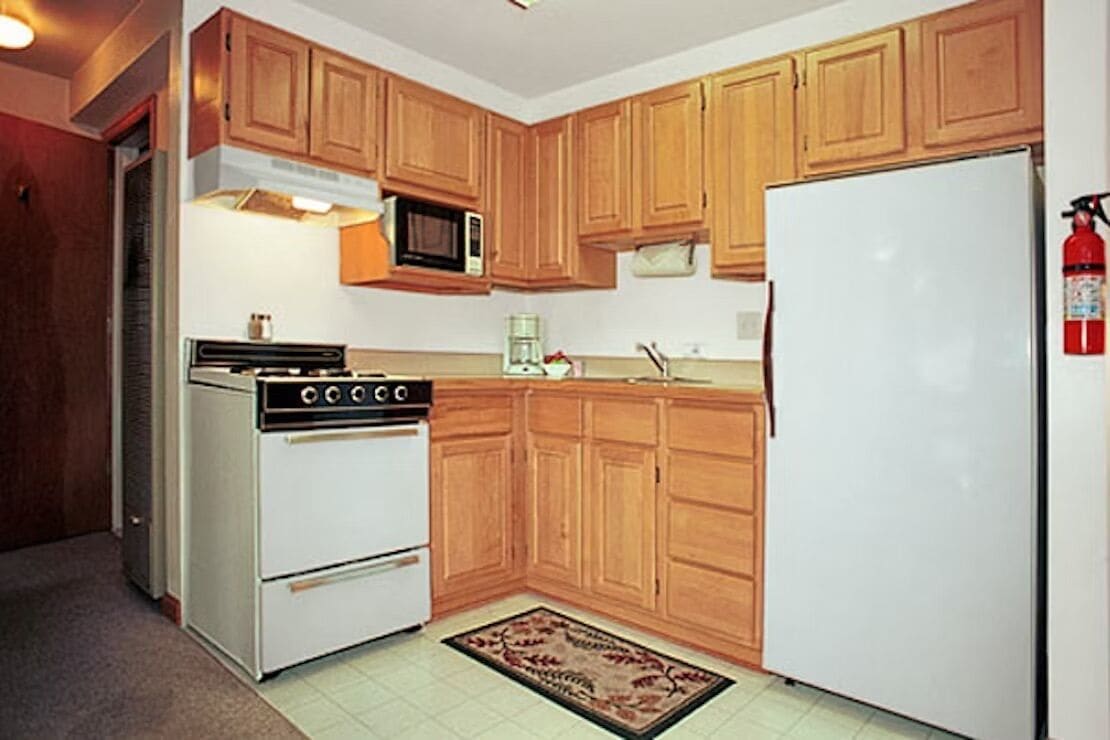 Eine Küche mit Holzschränken, einem weißen Kühlschrank, einem Herd und einer Mikrowelle.