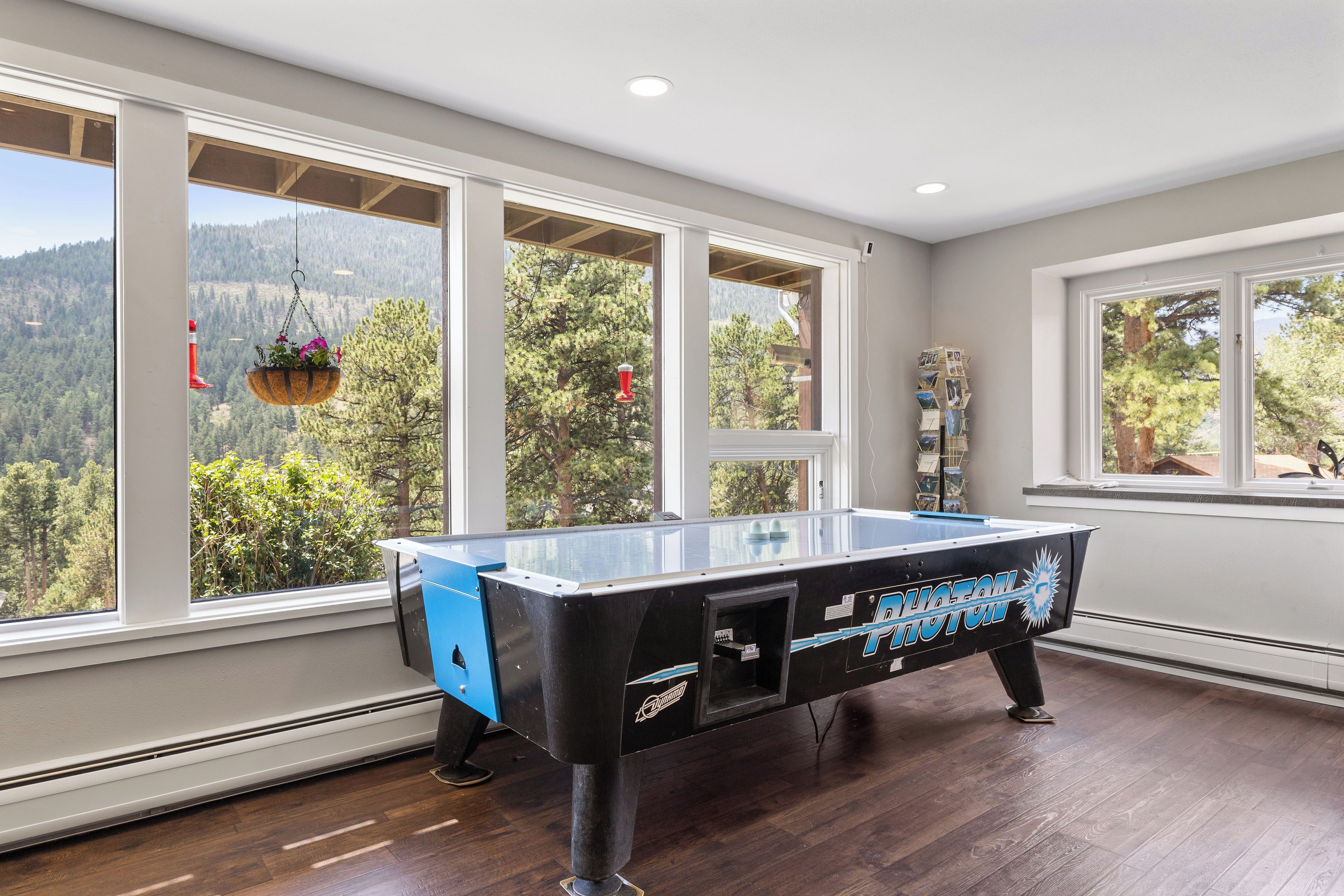 A pool table in a room with large windows overlooking a forested area.