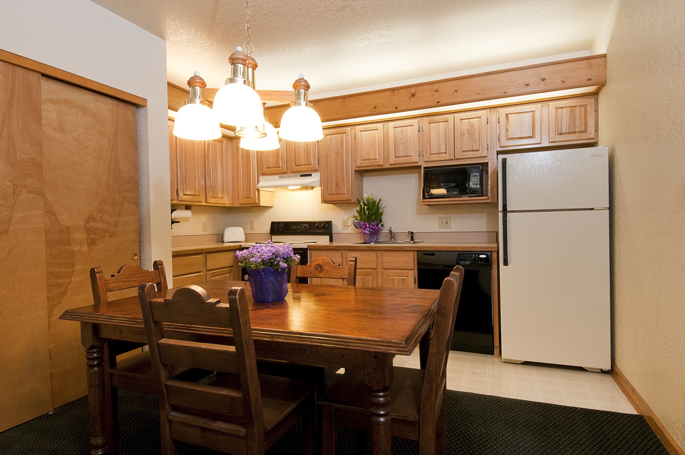 A kitchen with wooden cabinets, a refrigerator, a microwave, and a dining table with chairs.