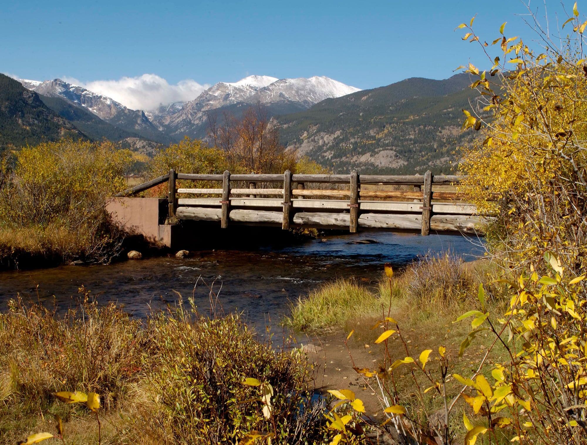 Un puente de madera sobre un río, con montañas al fondo.
